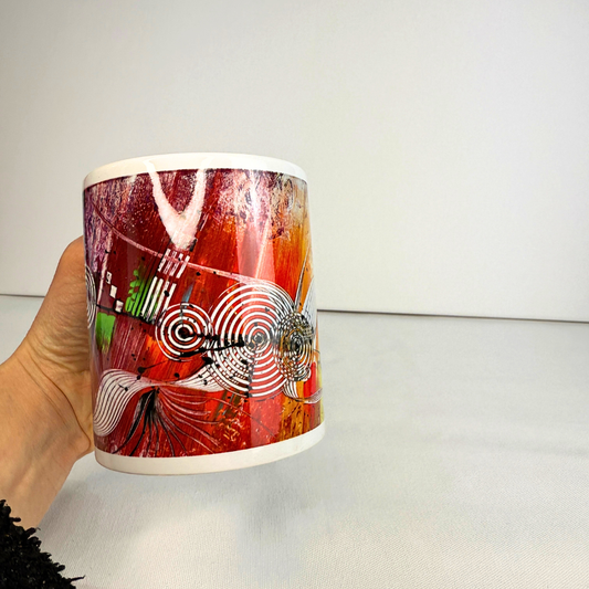 Hand hält bunte Kaffeetasse mit abstrakter moderner Kunst in kräftigen Farben.