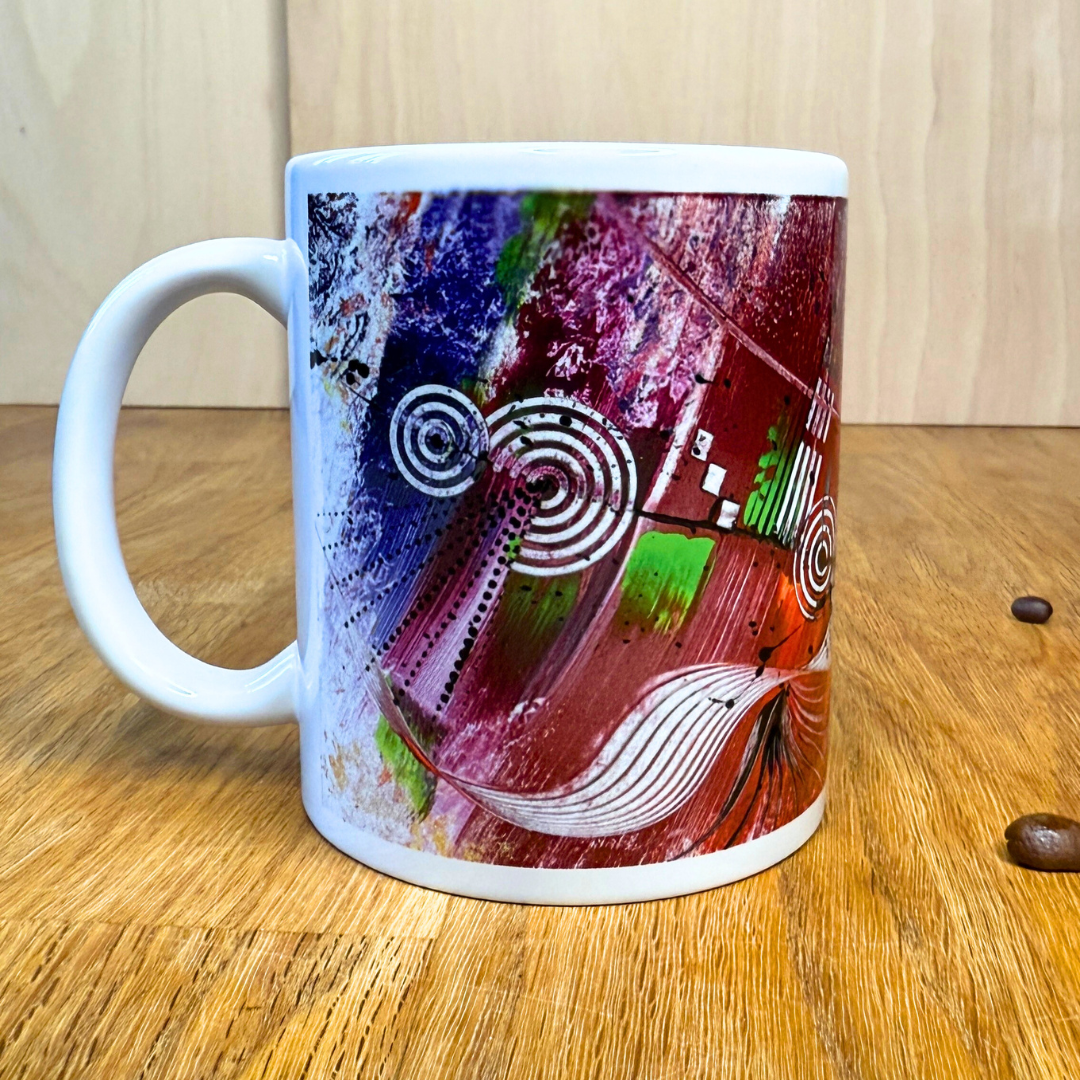Bunte Kaffeetasse mit modernem, abstraktem Kunstmotiv in kräftigen Multicolor-Tönen. Die Tasse steht auf einem Holztisch.