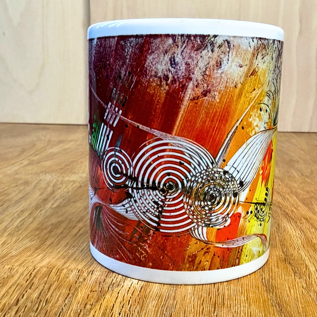Bunte Kaffeetasse mit modernem, abstraktem Kunstmotiv in kräftigen Multicolor-Tönen. Die Tasse steht auf einem Holztisch.